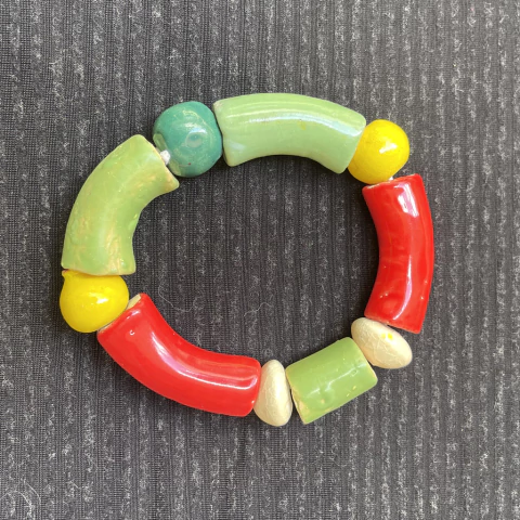 Pulseira de cerâmica colorida com elementos verdes, vermelhos, amarelos e creme, sobre fundo escuro.