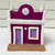 Miniatura de uma casa decorativa em tons de roxo e branco, com detalhes coloridos nas portas e um elemento decorativo na parte superior.