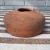 Vaso de cerâmica terracota com formato arredondado e bocal estreito, sobre um fundo de tecido listrado.