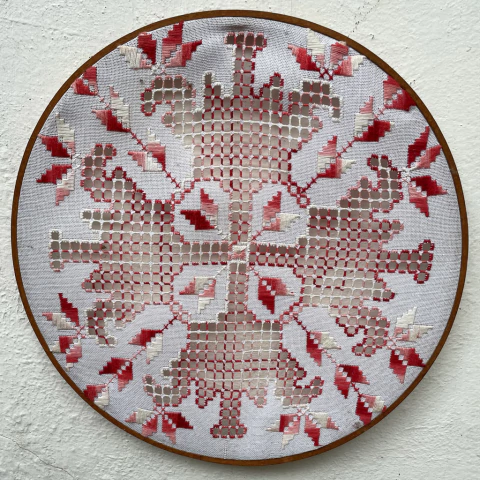 Quadro bastidor com bordado em tons de vermelho e branco, apresentando um padrão floral e geométrico.