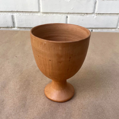 Um calice de cerâmica marrom, com base arredondada e corpo cilíndrico, ideal para uso utilitário ou como vaso.
