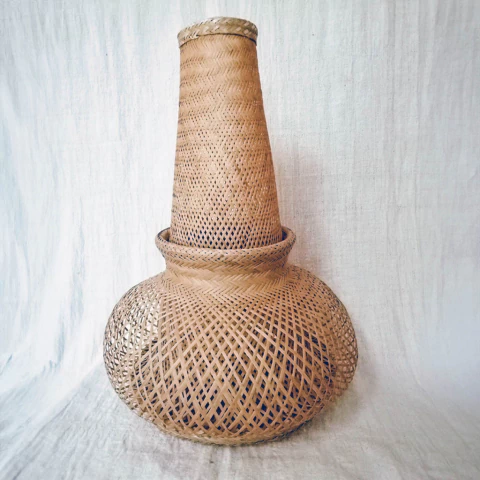 Vaso de palha trançada com formato alongado e base arredondada, exibindo detalhes de artesanato.