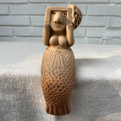 Estátua de cerâmica representando uma figura feminina com formato de sereia, destacando detalhes como a cauda escamosa e o cabelo trançado.