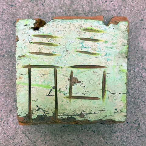 Casinha de parede com detalhes em verde e entalhes visíveis, representando o nome "Dedé".