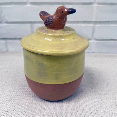 Recipiente de cerâmica com tampa amarela e detalhe de passarinho no topo.