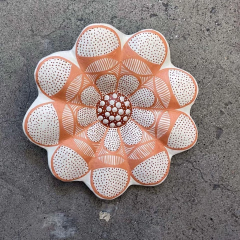 Prato decorativo em formato de flor com detalhes em tons de laranja e branco, apresentando padrões geométricos e bolinhas.