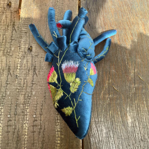 Coração decorativo de veludo azul com bordados florais coloridos, sobre superfície de madeira rústica