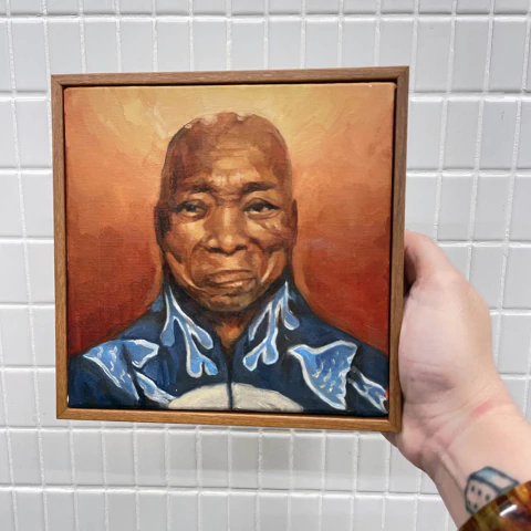 Pintura em tela retratando Milton Nascimento com fundo em tons de laranja e vermelho, moldura de madeira