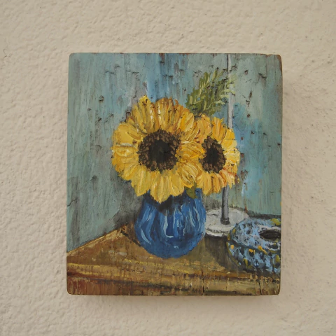 Pintura em madeira de dois girassóis em vaso azul com fundo azul e mesa de madeira
