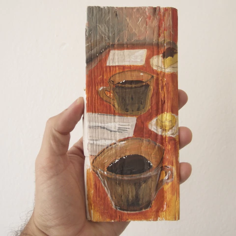 Pintura em madeira mostrando duas xícaras de café sobre uma mesa com guardanapo e prato com pão