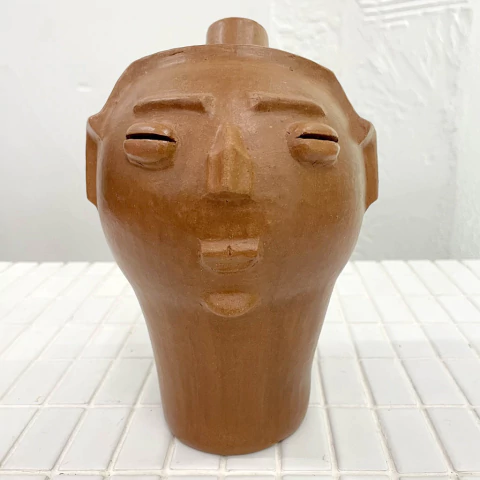 Escultura de cerâmica em forma de rosto humano, com detalhes esculpidos e coloração terra.