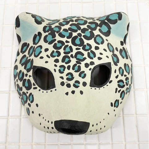 Máscara decorativa de um jaguar com manchas pretas e azul em fundo claro.
