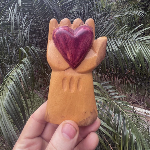 Escultura em madeira de uma mão segurando um coração vermelho esculpido