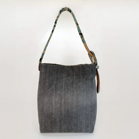 Bolsa jeans cinza com alça trançada colorida, ideal para uso diário.