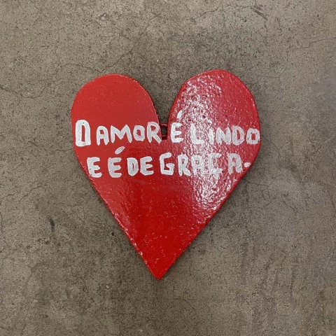 Coração vermelho com a frase "O amor é lindo e é de graça" pintada em branco.