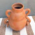 Vaso de cerâmica marajoara com duas alças, na cor terracota, sobre uma superfície de tecido listrado.