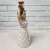 Estátua de cerâmica de uma mulher segurando um vaso na cabeça, vestida com um vestido branco com bolinhas marrons.
