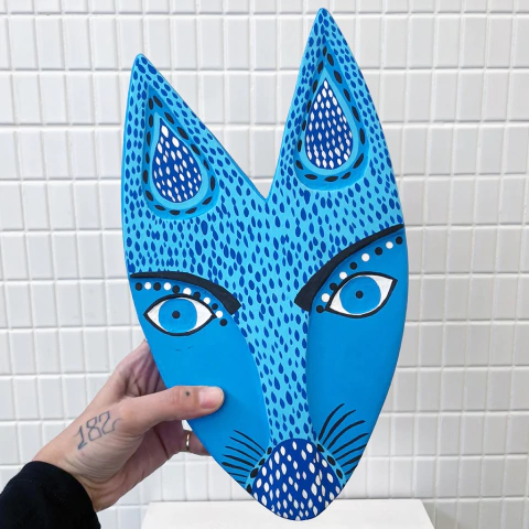 Máscara azul estilizada com formato de animal, destacando olhos grandes e detalhes em preto e branco.