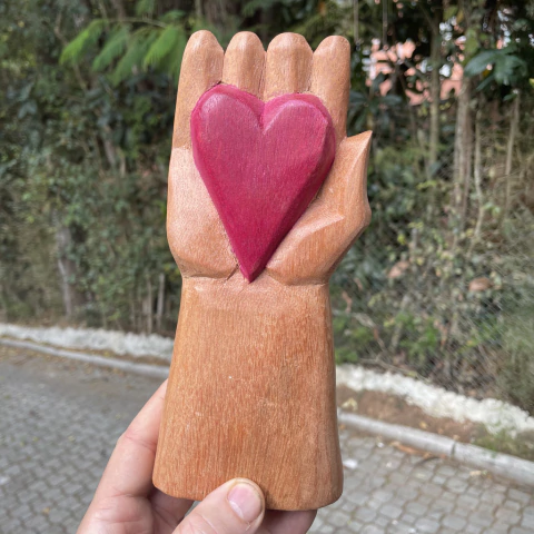 Escultura em madeira de uma mão segurando um coração vermelho