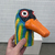 Escultura colorida de um pato com detalhes em azul, verde e laranja, sendo segurada por uma mão.