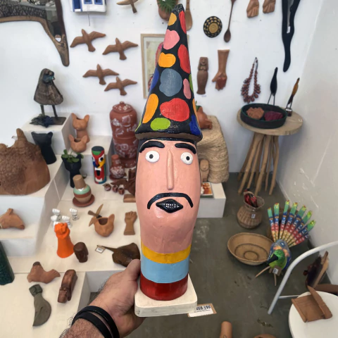 Escultura colorida de um personagem com chapéu pontudo e expressão facial intrigante, destacando-se pela pintura vibrante.