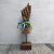 Escultura em madeira de uma mão com pulseiras coloridas e fitas, representando a figa.
