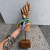 Escultura em madeira de uma mão com pulseiras coloridas e fitas, representando a figa.