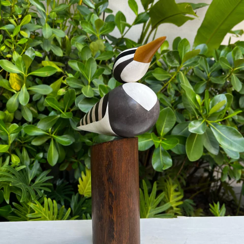 Escultura de um pássaro em madeira, com detalhes em preto e branco, montada sobre uma base de madeira escura.