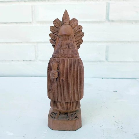 Escultura em madeira de figura humana com penacho e vestimenta tradicional.