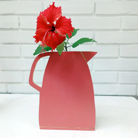 Vaso de Ilusão na cor rosa com flor vermelha de hibisco e folhas verdes, em fundo branco.