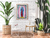 Uma sala de estar com uma planta grande, uma cadeira moderna e uma mesa de centro, apresentando uma obra de arte colorida na parede.
