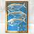 Quadro decorativo com estampa de peixes em fundo azul, com a frase "O mar começava todos os dias de novo".