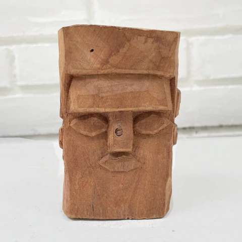 Escultura em madeira representando um rosto estilizado com traços marcantes.