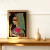 Quadro decorativo com uma mulher vestindo roupas coloridas, segurando uma flor, em um ambiente minimalista.