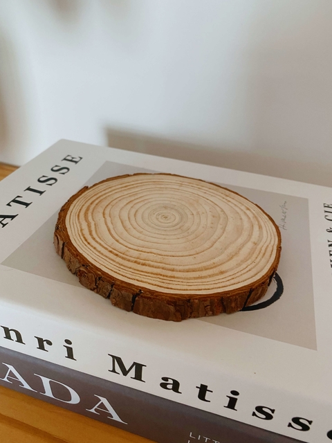 Base decorativa redonda de madeira com anéis de crescimento visíveis, sobre livro branco e cinza