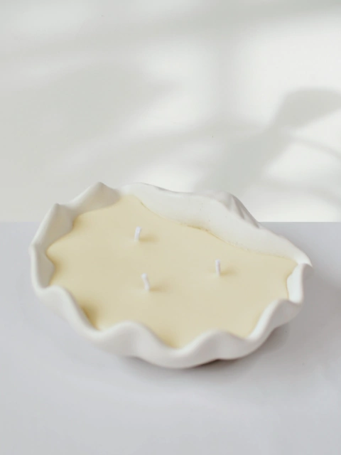 Vela aromática em formato de concha grande, com três pavios, na cor creme.
