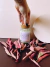 Uma vela aromática de lavanda em um pote de vidro com tampa de cortiça, cercada por folhas secas em tons de rosa.