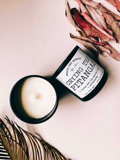 Vela aromática de pitanga negra da Gringo Collection em recipiente preto, com tampa removida e folhas secas decorativas ao lado