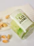 Vela aromática Pistacchio em copo de vidro com rótulo verde claro e pistaches espalhados ao fundo