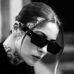 Modelo usando óculos de sol Double X, com design retangular e detalhes de tatuagens visíveis.