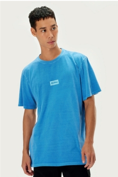 Modelo usando camiseta azul com estampa discreta, em fundo neutro.
