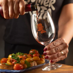 Taça de vinho Bohemia Mulher Preta sendo servida com vinho tinto ao lado de prato com tomates e ervas frescas