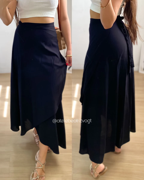 Saia envelope preta em tecido leve, com detalhe assimétrico, usada por uma modelo em ambiente interno.