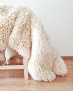 Alfombra de cuero de oveja irregular en color blanco, con textura suave y esponjosa, colocada sobre una silla de madera.