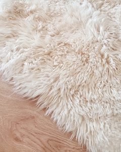 Alfombra de cuero de oveja Sarakina de color blanco, con textura suave y peluda, sobre un suelo de madera clara.