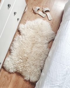 Alfombra de corderito de cuero de oveja color natural, tamaño extra large, colocada en un ambiente acogedor junto a unas sandalias.
