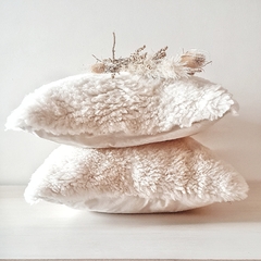 Almohadones de cuero de oveja con pelo en color blanco, apilados y decorados con flores secas.
