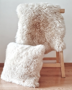 Almohadón de 50x50 cm y corderito de 80x50 cm de cuero de oveja sobre una silla de madera.