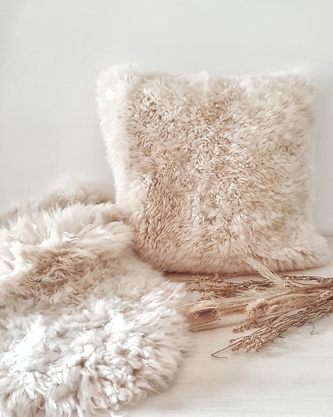 Almohadón de cuero de oveja de 50x50 cm y corderito de 80x50 cm sobre una superficie clara, decorados con ramas secas.
