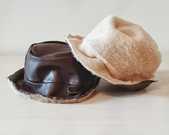 Dos sombreros de cuero, uno marrón y otro blanco, sobre una superficie clara.